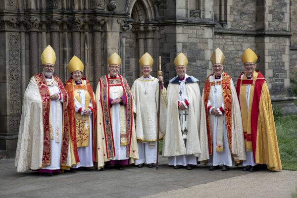 Seven bishops in full ceremonial vestments and mitres posing outside a cathedral